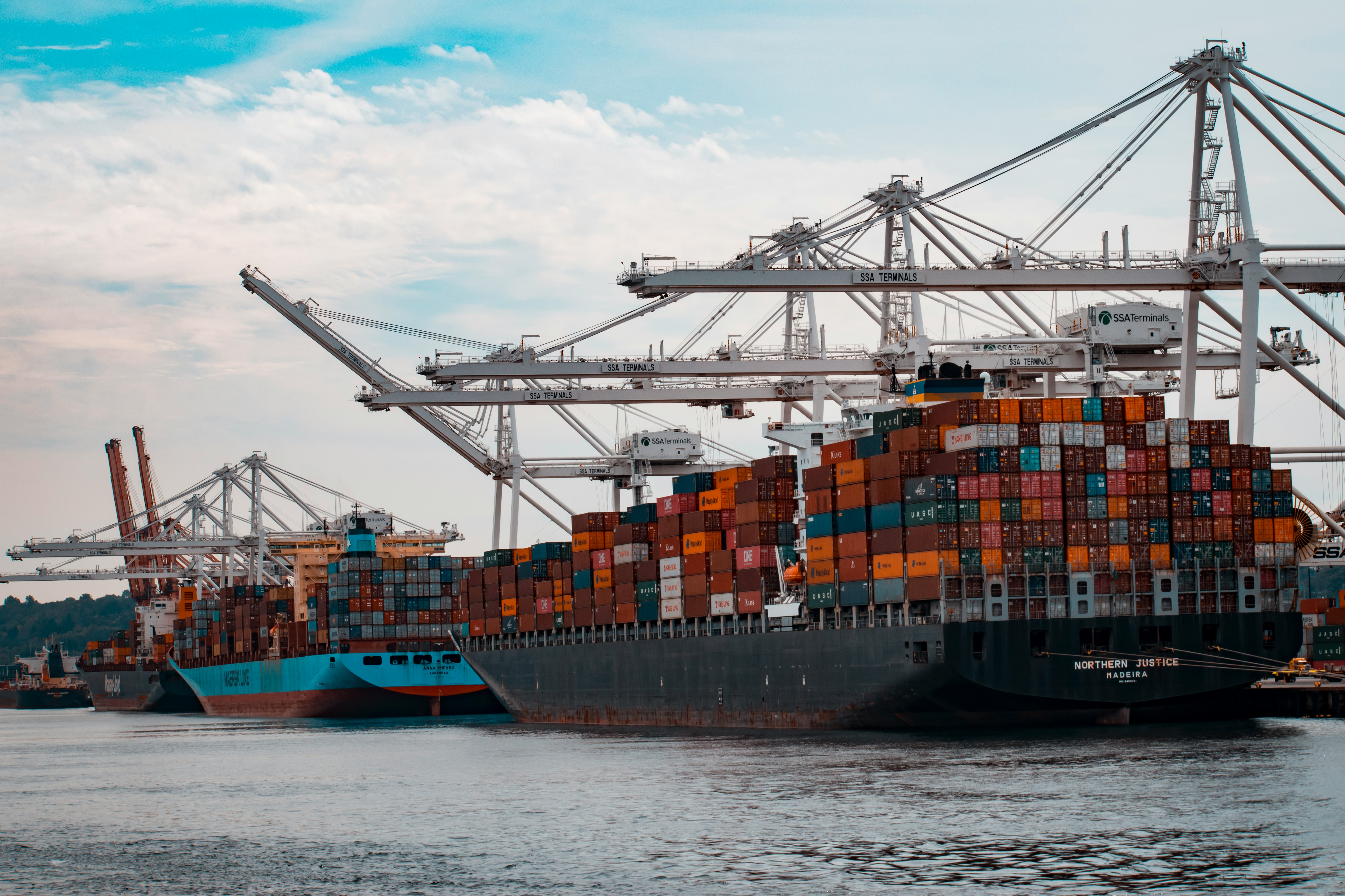 Port crane lifting a shipping container above stacked freight